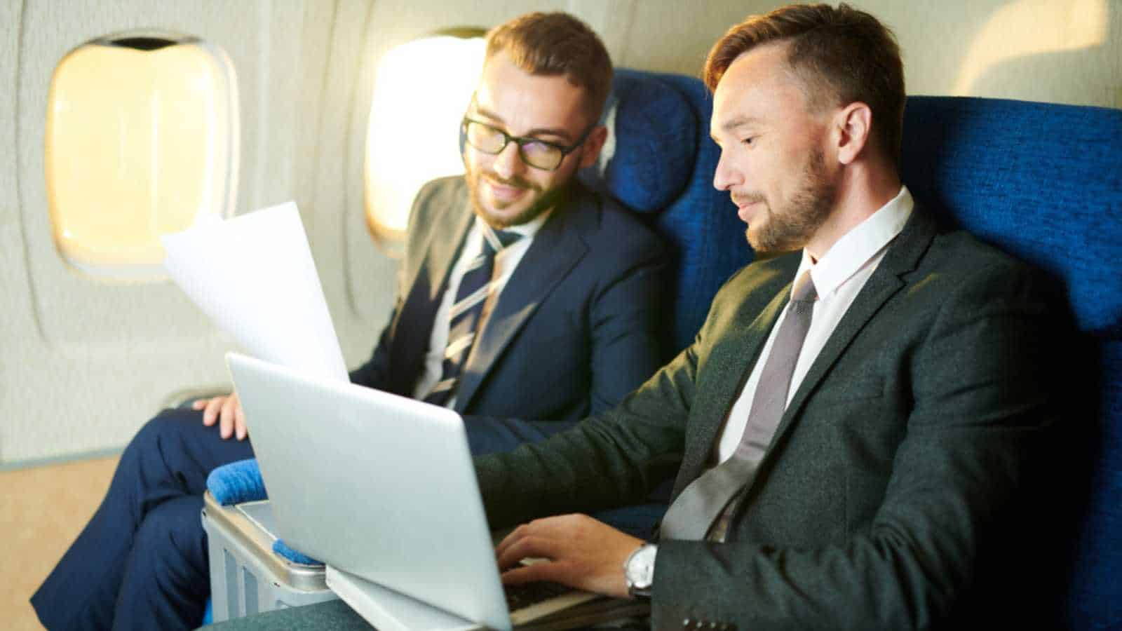 Portrait of two successful businessmen using laptop and working while enjoying first class flight in plane copy space