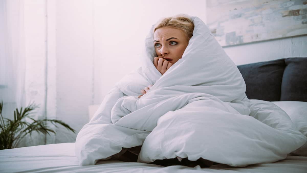 scared woman on bed covered in blanket