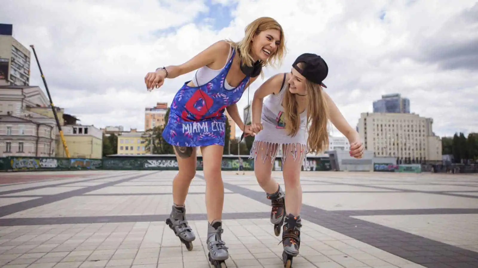 Two young beautiful blonde hipster girls on summer day having fun in european city roller-skating