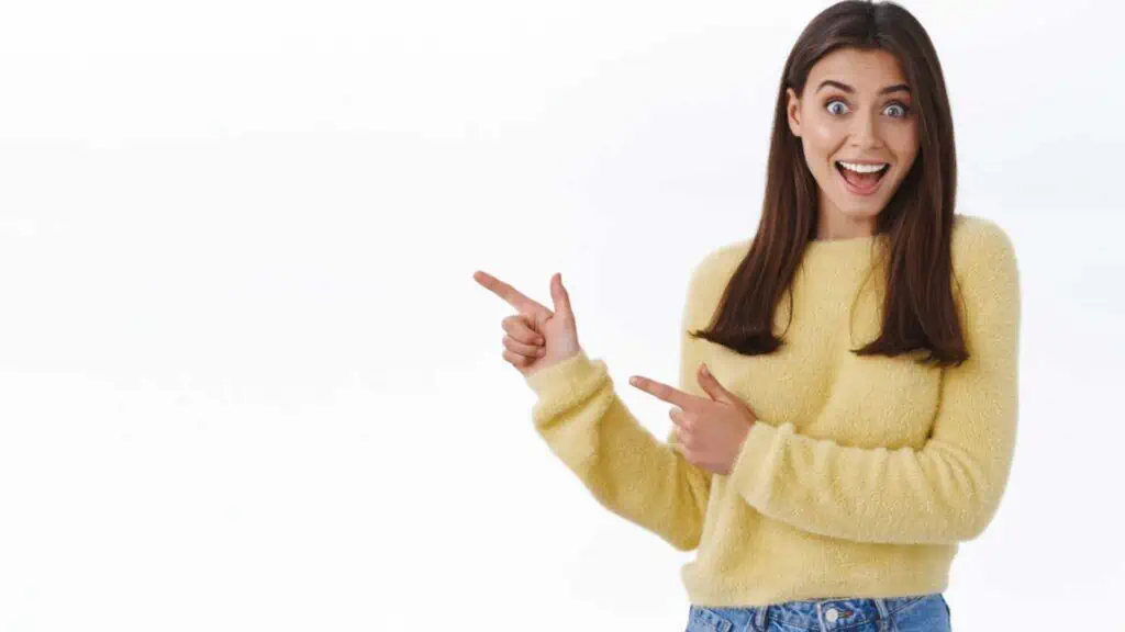 Great news hey take look. Excited happy and surprised beautiful young woman in yellow sweater turn yout attention at banner, pointing fingers left and scream joyful, stand white background