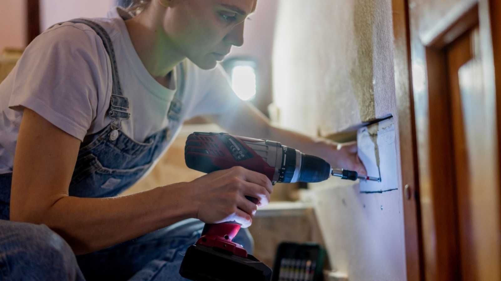 Young pretty woman doing wall repair at home using screwdriver