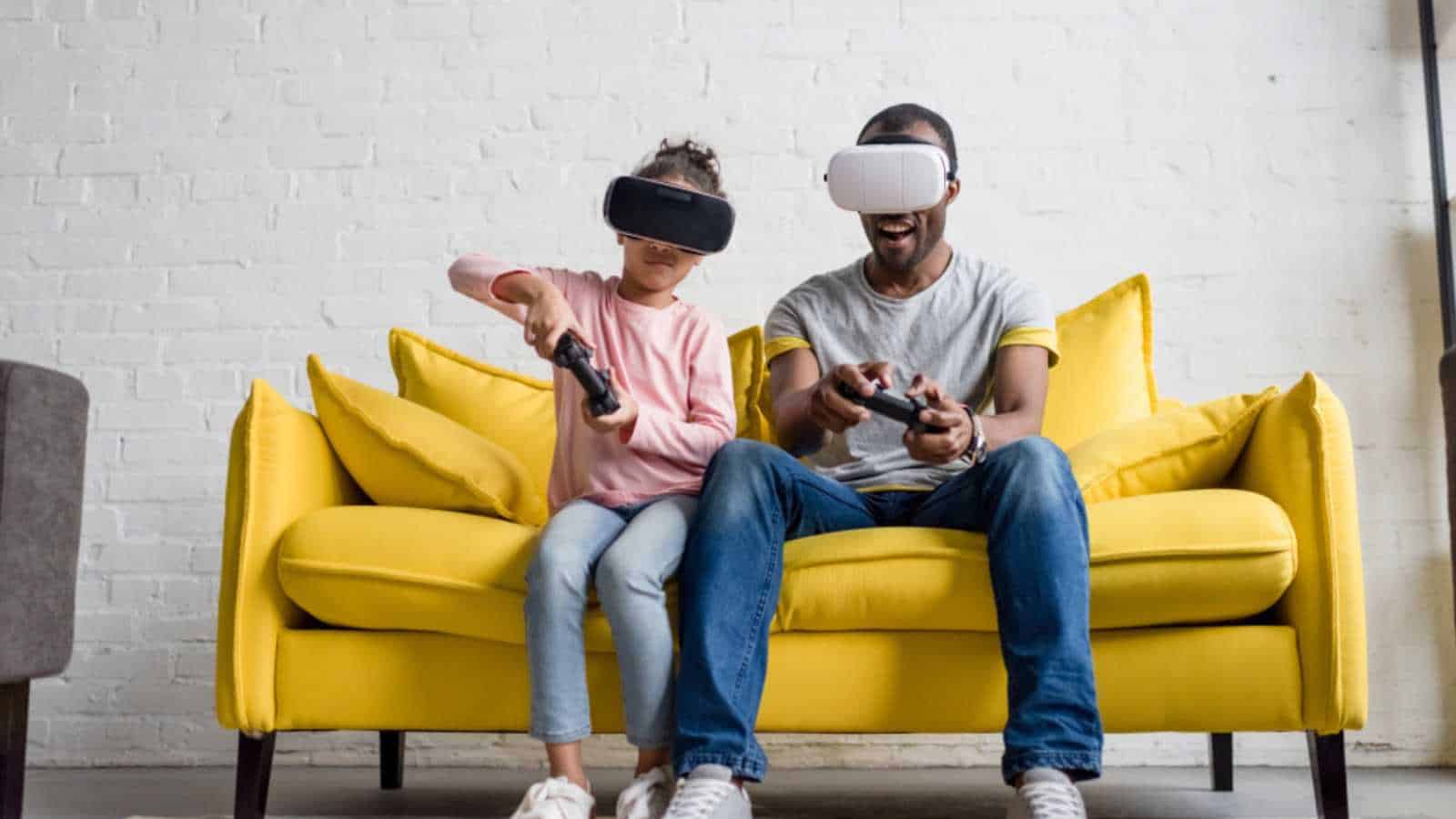 father and daughter in vr headsets playing video games on couch at home