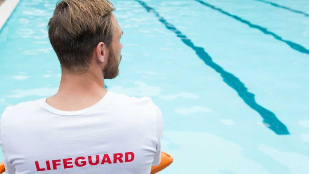Rear view of lifeguard sitting on chair with rescue buoy at poolside
