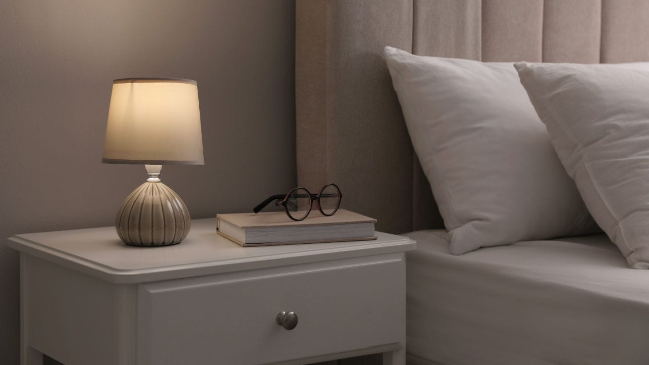 Stylish lamp, book and glasses on bedside table indoors