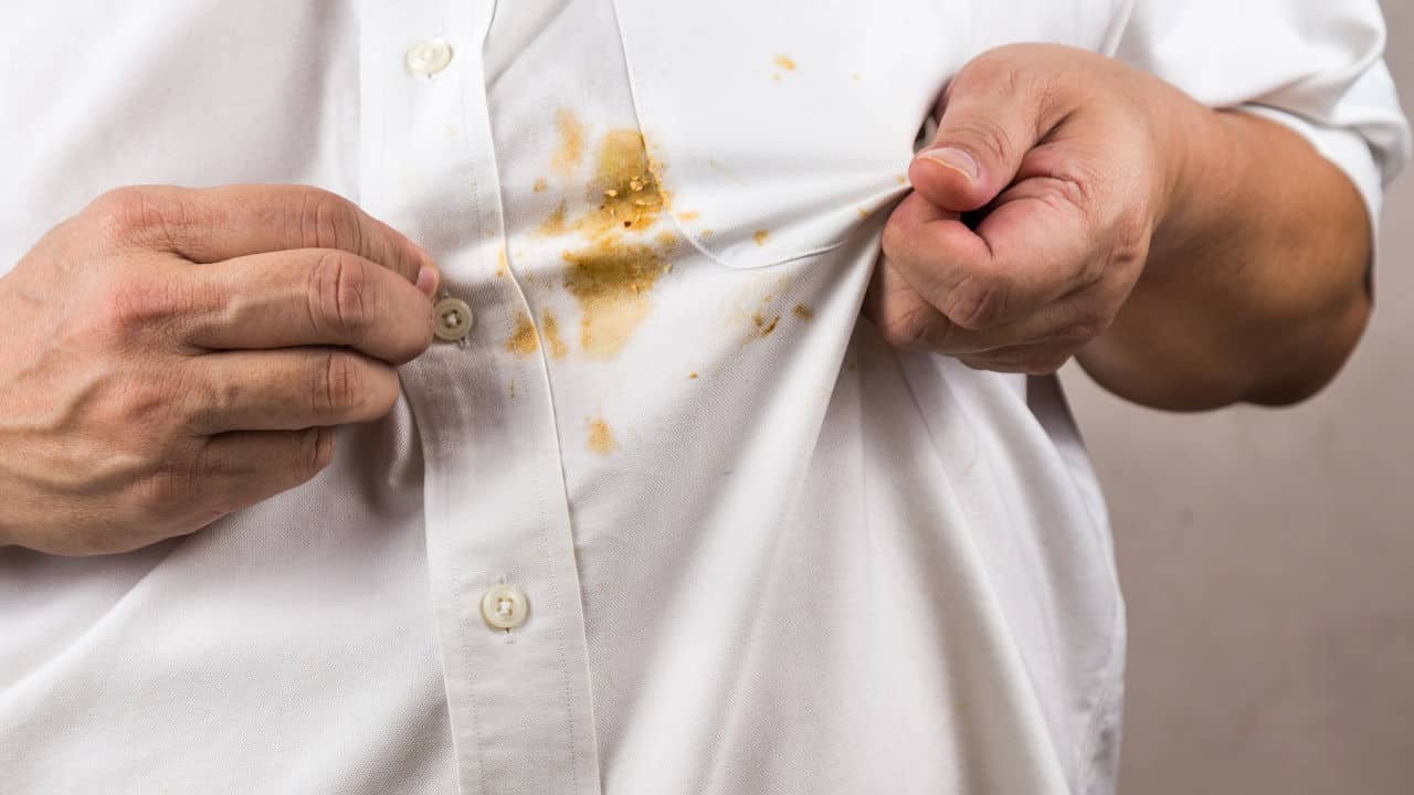 Frustrated person pointing to spilled curry stain on white shirt