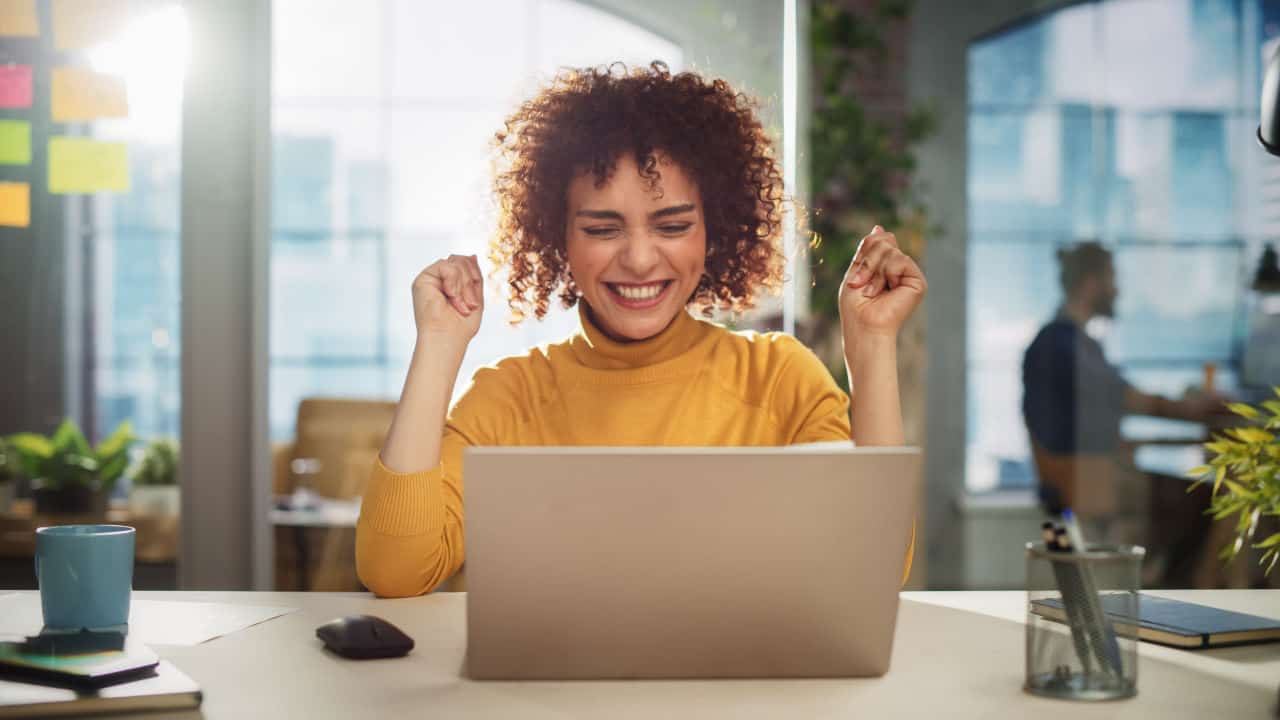 woman excited sitting at her desk on her laptop
