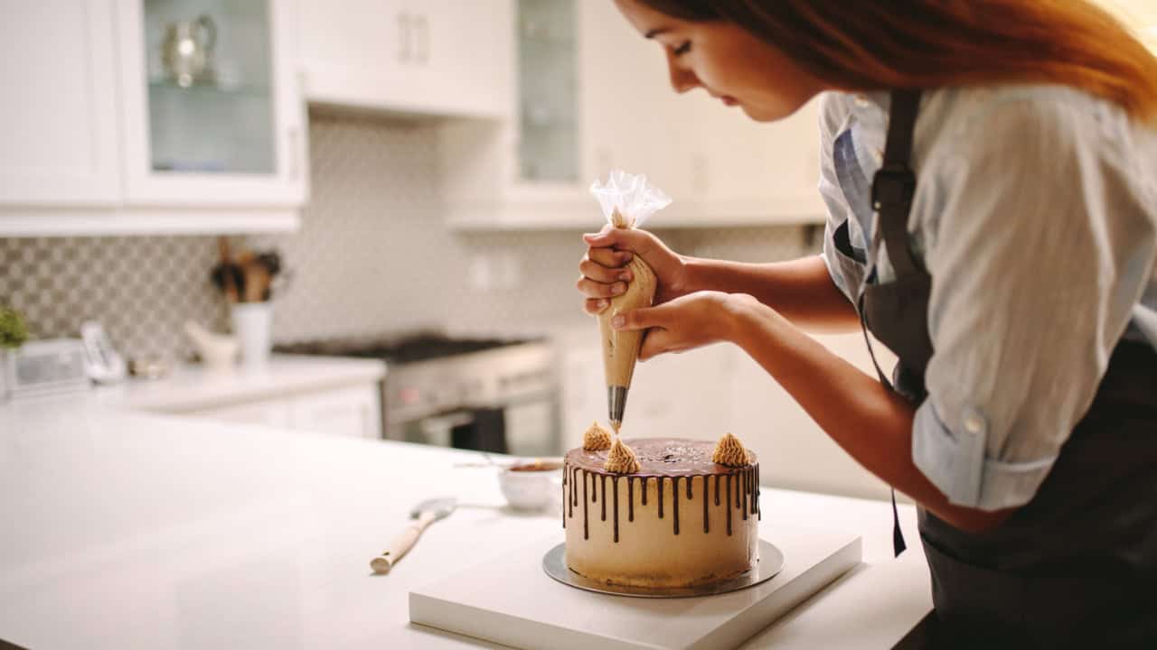 Female wearing a apron decorating cake with a pastry bag with cream