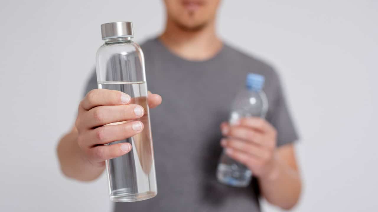 young man comparing water in reusable glass and plastic bottle