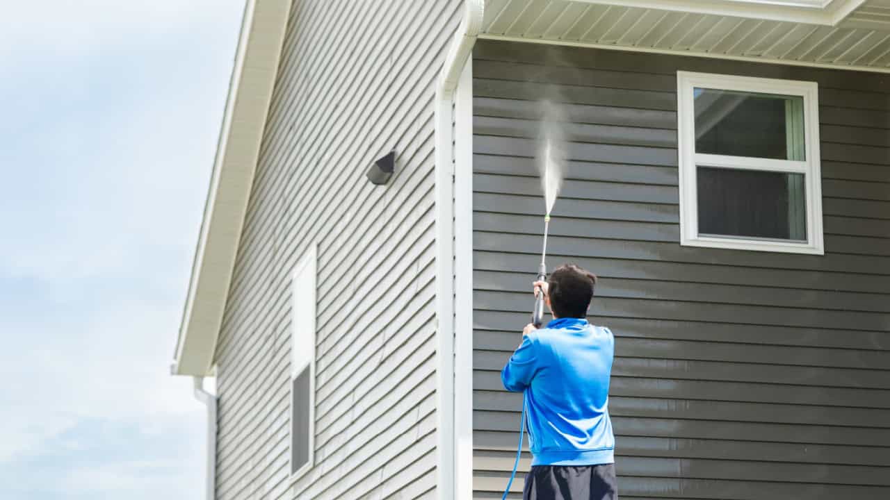 Man in blue jacket cleans dusk and dirt from exterior siding