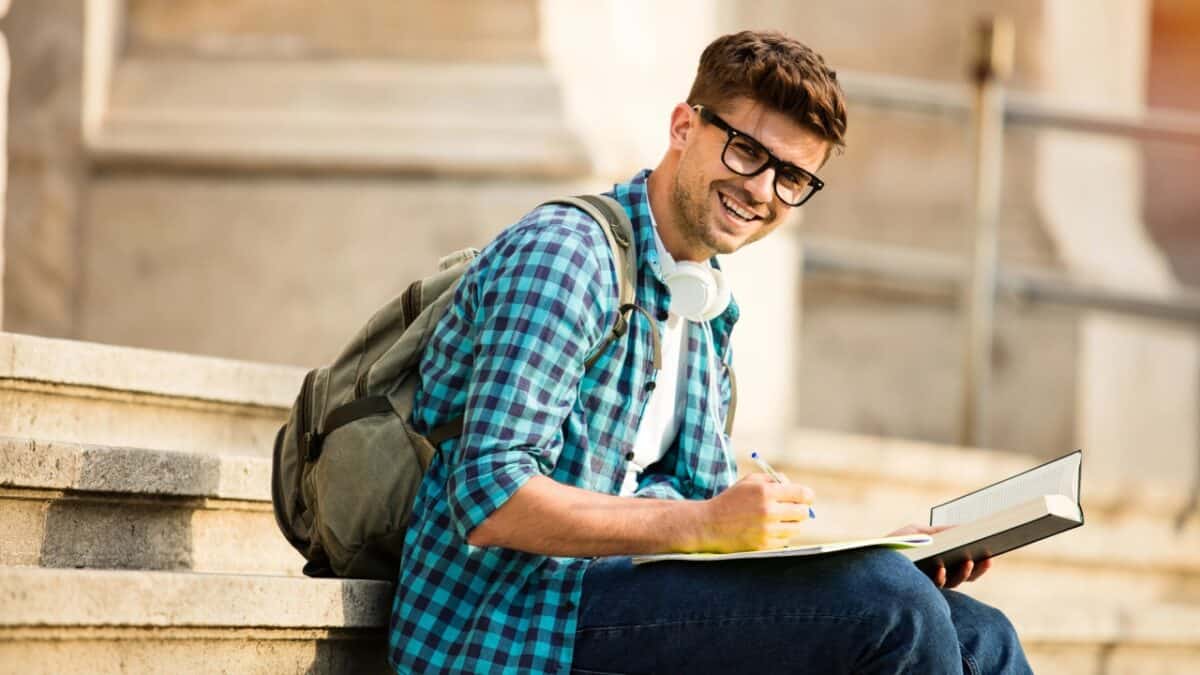 Young student with glasses standing on stairs of school or university