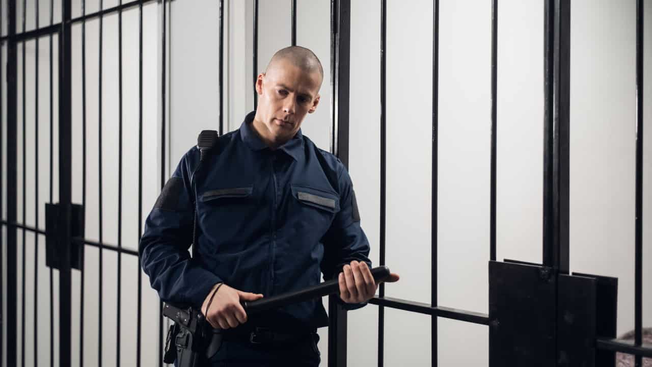 A strict prison guard in uniform guards cells with prisoners