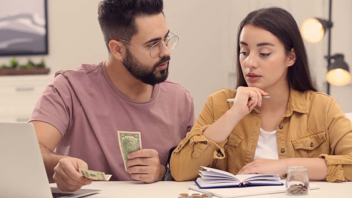 Young couple counting money at white table indoors