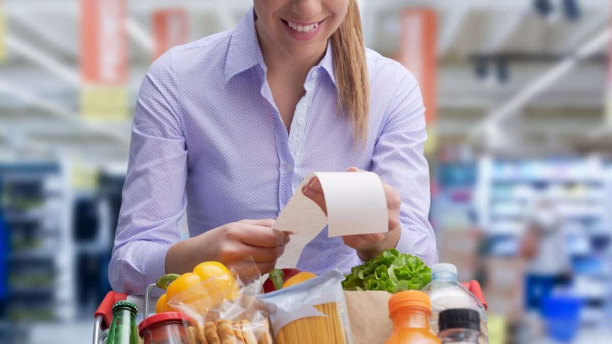 Smiling woman leaning on the shopping cart and checking the grocery receipt